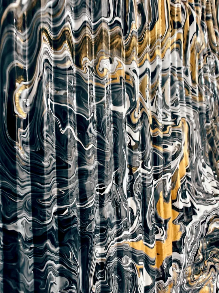 A close view of a poured painting whose surface has pleated into vertical bands: black, white and gold marbling folded like curtain pleats, with a broad seam of gold running down the right side.