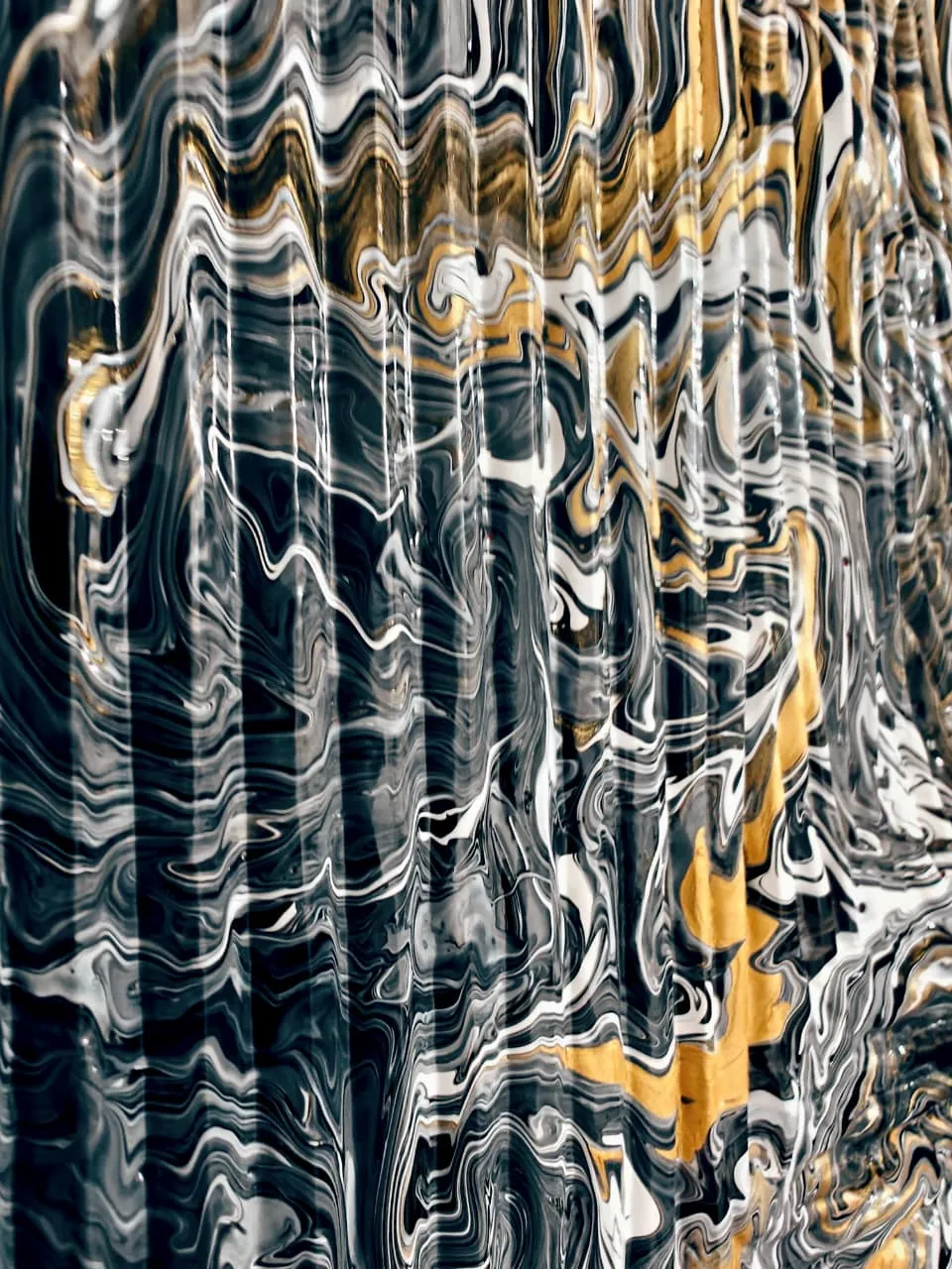 A close view of a poured painting whose surface has pleated into vertical bands: black, white and gold marbling folded like curtain pleats, with a broad seam of gold running down the right side.
