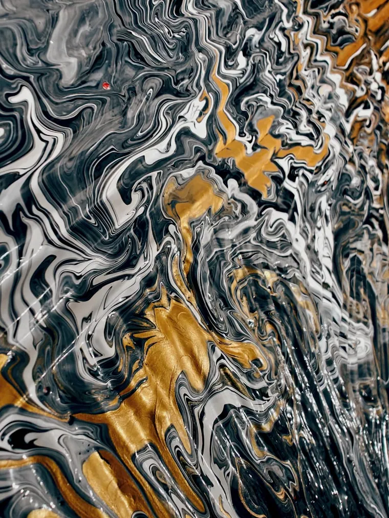 A poured painting seen at an angle: marbled black and white swirls with thick bands of metallic gold folded through the lower half, the surface rippled and glossy, a single red fleck near the top.